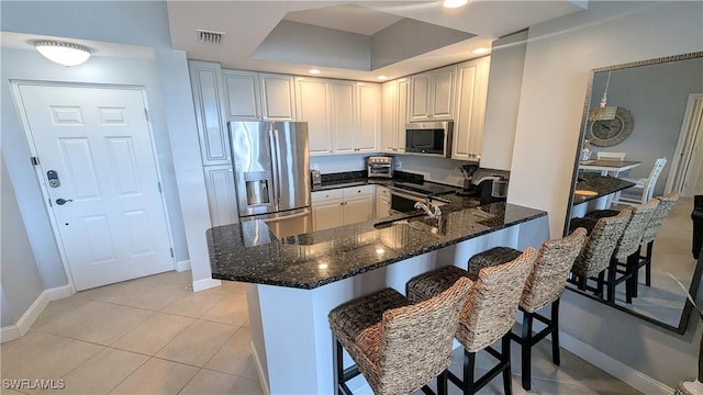 kitchen featuring stainless steel appliances, a peninsula, a sink, visible vents, and dark stone countertops