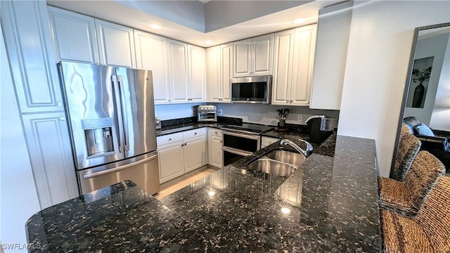 kitchen featuring dark stone counters, stainless steel appliances, a sink, and white cabinetry