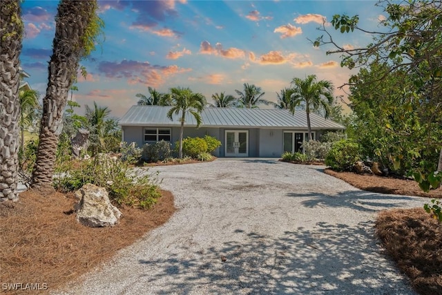 ranch-style house with stucco siding, a standing seam roof, french doors, gravel driveway, and metal roof