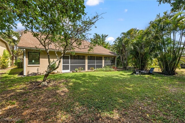 7735 Citrus Hill Ln, Naples, FL 34109 - back of house featuring an outdoor fire pit, a lawn, stucco siding, and a sunroom
