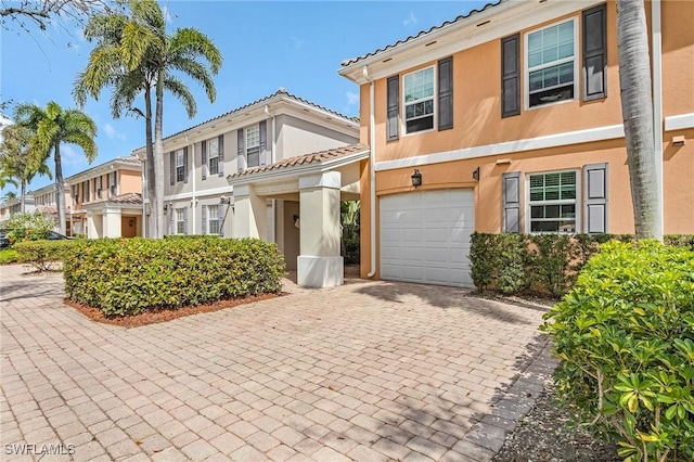 view of front facade featuring decorative driveway, a tile roof, stucco siding, a garage, and a residential view