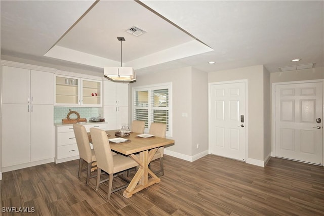 dining space featuring dark wood-style floors, a tray ceiling, visible vents, and baseboards