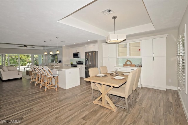 dining space with ceiling fan, recessed lighting, wood finished floors, visible vents, and a tray ceiling