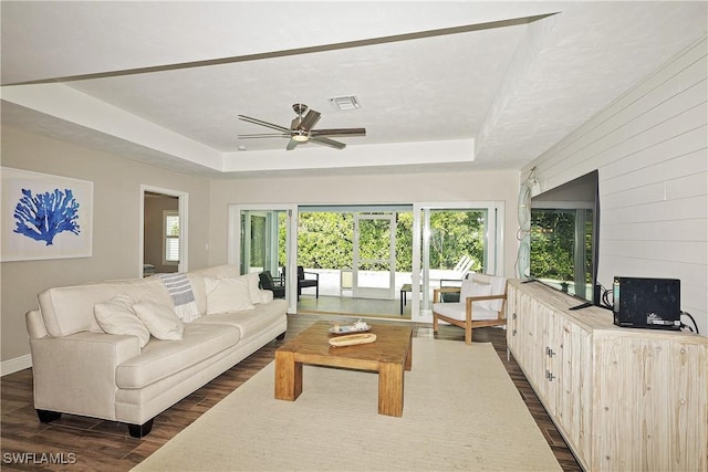 living area with baseboards, visible vents, a raised ceiling, ceiling fan, and dark wood-style flooring