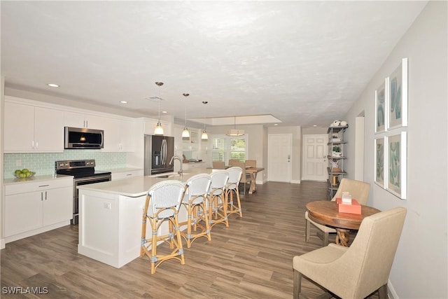 kitchen with a center island with sink, light wood finished floors, light countertops, decorative backsplash, and appliances with stainless steel finishes