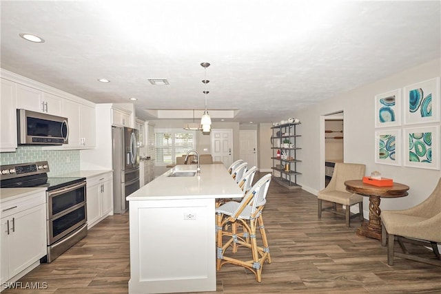 kitchen with a breakfast bar, visible vents, appliances with stainless steel finishes, decorative backsplash, and dark wood finished floors