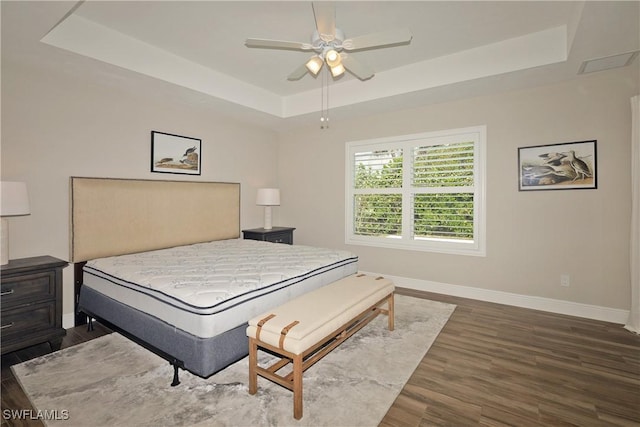 bedroom featuring a tray ceiling, wood finished floors, a ceiling fan, and baseboards