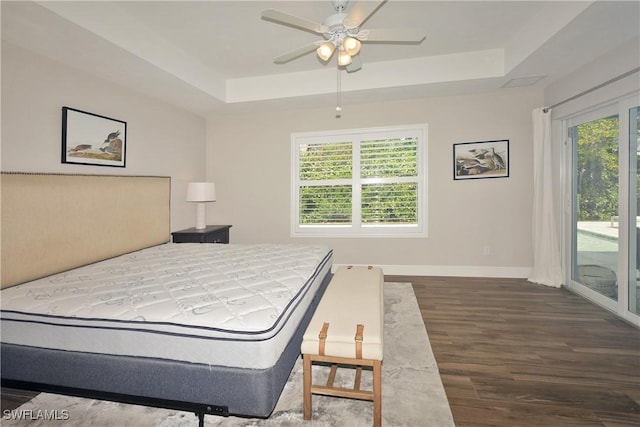 bedroom with access to outside, multiple windows, a tray ceiling, and wood finished floors