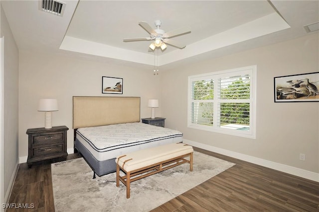 bedroom featuring dark wood-style floors, a raised ceiling, visible vents, and baseboards