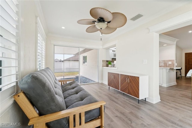 living area featuring visible vents, ornamental molding, light wood-style floors, a ceiling fan, and baseboards