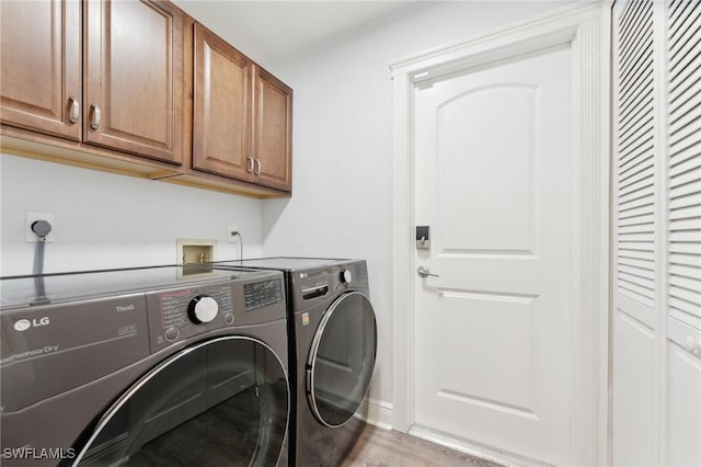 laundry area with light wood-type flooring, cabinet space, and washing machine and clothes dryer