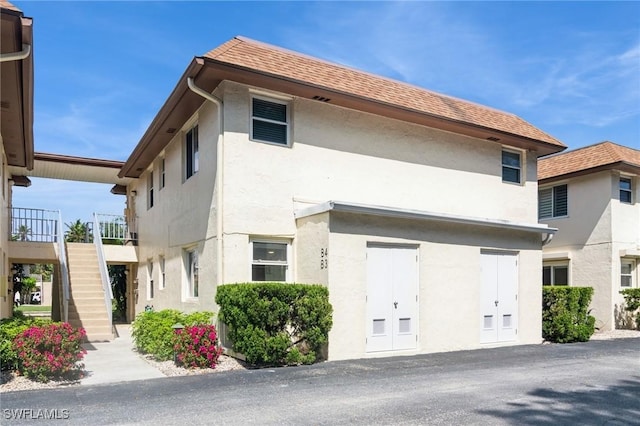 view of front of home with roof with shingles, stairway, and stucco siding