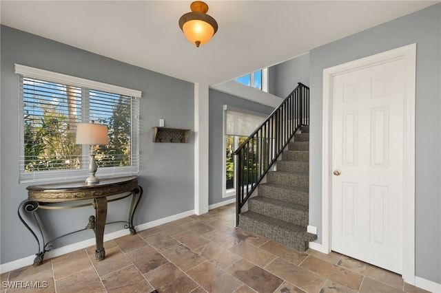 entryway featuring stone finish flooring, plenty of natural light, baseboards, and stairs