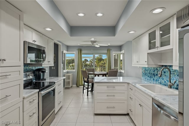 kitchen featuring glass insert cabinets, a peninsula, stainless steel appliances, white cabinetry, and a sink