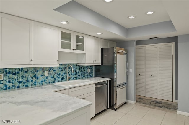 kitchen featuring a tray ceiling, glass insert cabinets, white cabinets, a sink, and dishwasher