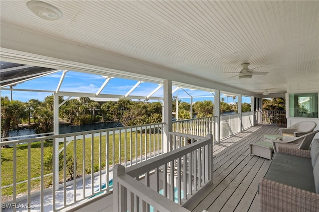 wooden terrace featuring a water view, glass enclosure, ceiling fan, and a yard