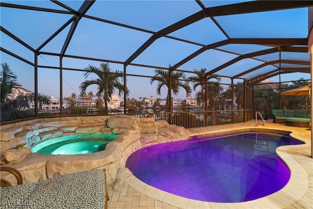 pool at dusk with glass enclosure, an outdoor pool, a patio, and an in ground hot tub