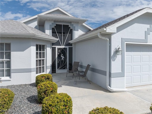 view of exterior entry with a garage, a shingled roof, and stucco siding