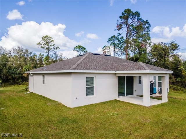 rear view of property with a shingled roof, a patio area, a yard, and stucco siding