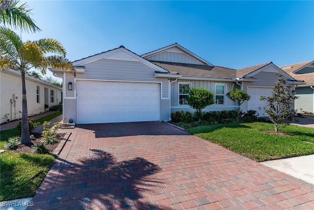 single story home with a garage, a tile roof, decorative driveway, board and batten siding, and a front yard