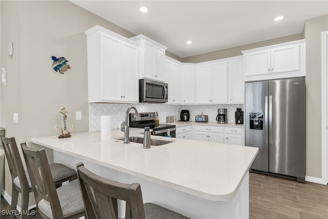 kitchen featuring stainless steel appliances, tasteful backsplash, white cabinetry, a sink, and a peninsula