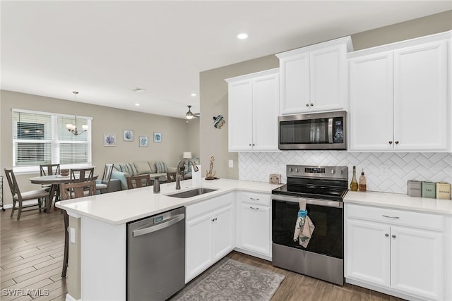 kitchen with a peninsula, stainless steel appliances, light countertops, white cabinetry, and a sink