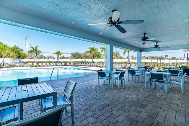 view of patio featuring ceiling fan, a community pool, fence, and outdoor dining space