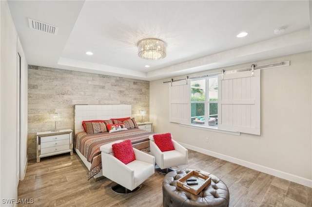bedroom with an accent wall, visible vents, baseboards, and wood finished floors
