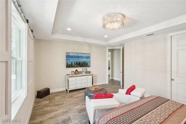 bedroom with a tray ceiling, recessed lighting, visible vents, light wood-type flooring, and baseboards