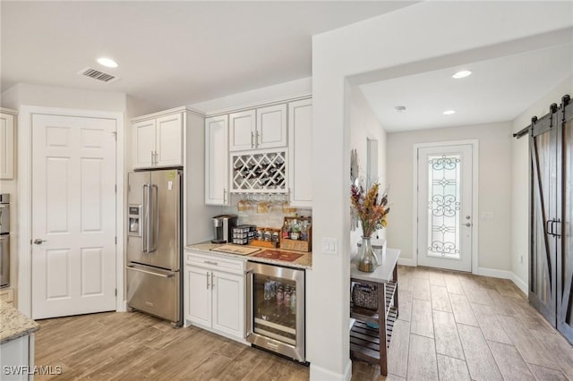 kitchen with light stone counters, wine cooler, a barn door, high end refrigerator, and visible vents