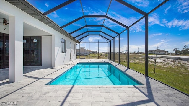 outdoor pool with a ceiling fan, glass enclosure, a patio area, and a lawn