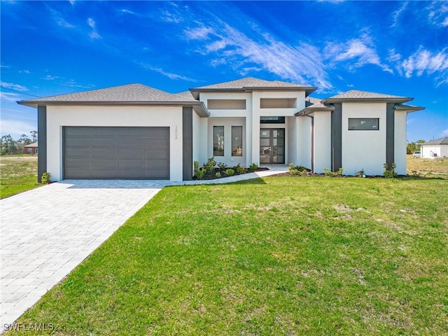 prairie-style home with a garage, decorative driveway, a front yard, and stucco siding