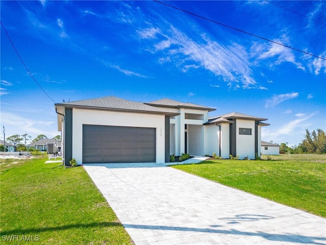 prairie-style home with a front yard, decorative driveway, an attached garage, and stucco siding