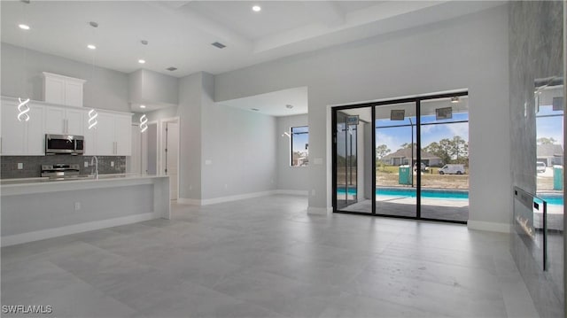 kitchen with tasteful backsplash, a towering ceiling, appliances with stainless steel finishes, open floor plan, and white cabinetry