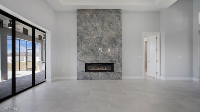 unfurnished living room featuring a high end fireplace, baseboards, and a high ceiling