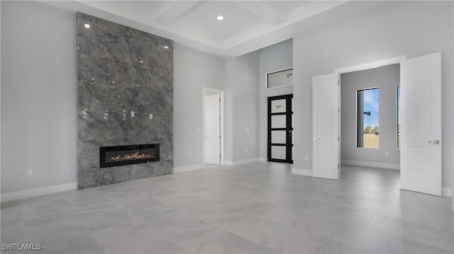 unfurnished living room featuring baseboards, coffered ceiling, a high ceiling, a fireplace, and beam ceiling