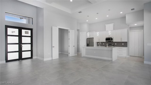 kitchen featuring a towering ceiling, white cabinets, french doors, appliances with stainless steel finishes, and a center island with sink