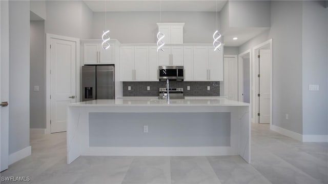 kitchen with stainless steel appliances, a large island with sink, light countertops, white cabinetry, and backsplash