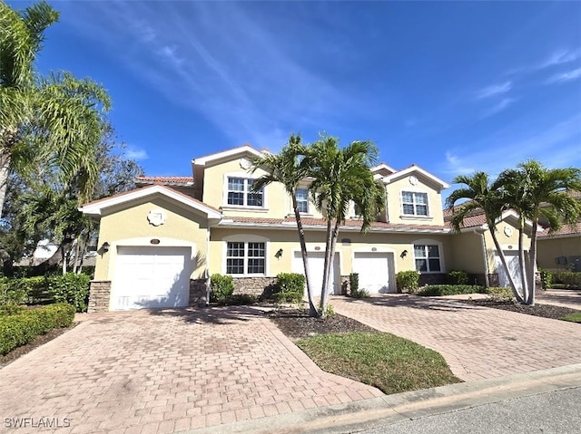 view of front of home with an attached garage, a tile roof, stone siding, decorative driveway, and stucco siding