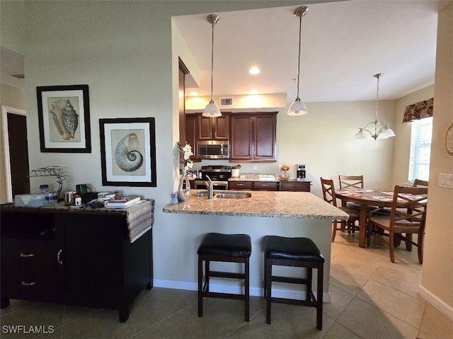 kitchen with a peninsula, a sink, stainless steel microwave, a kitchen bar, and pendant lighting