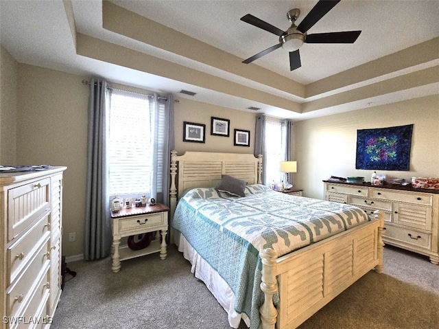 bedroom featuring visible vents, a raised ceiling, a ceiling fan, and dark colored carpet