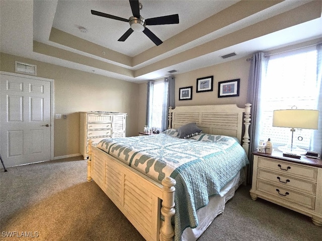 bedroom with ceiling fan, visible vents, a tray ceiling, and dark carpet