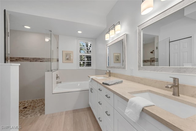 bathroom featuring a walk in shower, wood finished floors, a sink, and a garden tub