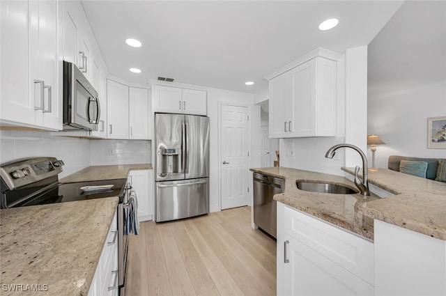 kitchen featuring white cabinets, light stone counters, appliances with stainless steel finishes, light wood-style floors, and a sink