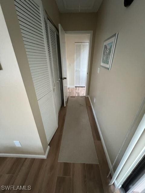 corridor with dark wood-type flooring, attic access, and baseboards