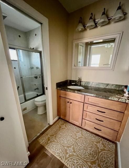 bathroom featuring baseboards, toilet, wood finished floors, combined bath / shower with glass door, and vanity