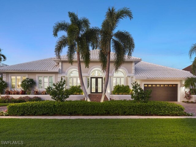 view of front of house with an attached garage, stucco siding, a front lawn, and french doors