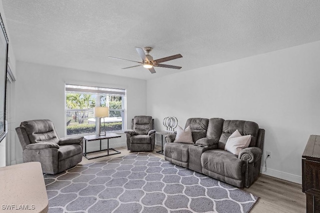 living area featuring a ceiling fan, a textured ceiling, baseboards, and wood finished floors