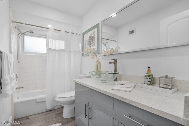 bathroom with toilet, wood finished floors, vanity, visible vents, and shower / bathtub combination with curtain