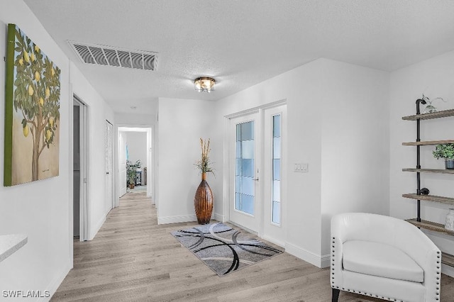 foyer entrance featuring a textured ceiling, light wood finished floors, visible vents, and baseboards